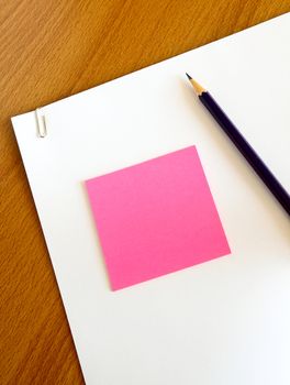 white paper with pencil and pink memo on wood table