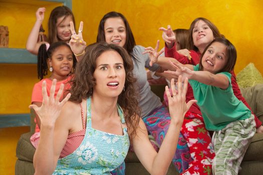 Unhappy mom among wild little girls with hands up in frustration