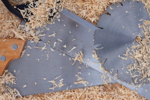 Background with softwood shavings and steel of circular saw blade and two handsaws all with sharp teeth.