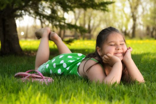 A young girl laying in the grass relaxing and enjoying the spring weather.