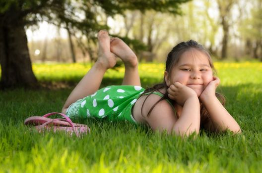 A young girl laying in the grass relaxing and enjoying the spring weather.