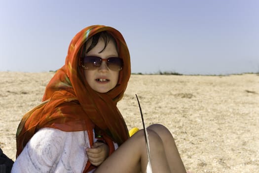 The girl with a feather sits on sand 