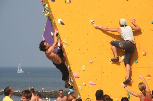 Annual Bouldering Competition on Scheveningen beach. Participants climbing artificial rock face. 