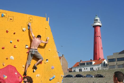 Annual Bouldering Competition on Scheveningen beach. Participant climbing artificial rock face with backdrop of Scheveningen lighthouse