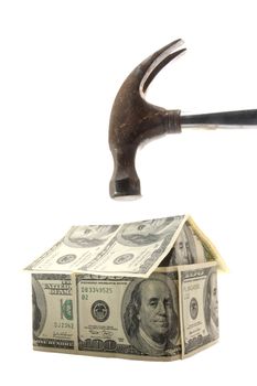 Hammer about to smash a home made out of US $100 bills - concept photo of home mortgage crisis