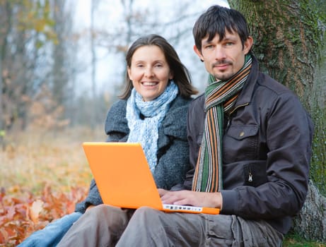 Romantic mature couple sitting with laptop in the autumn park.