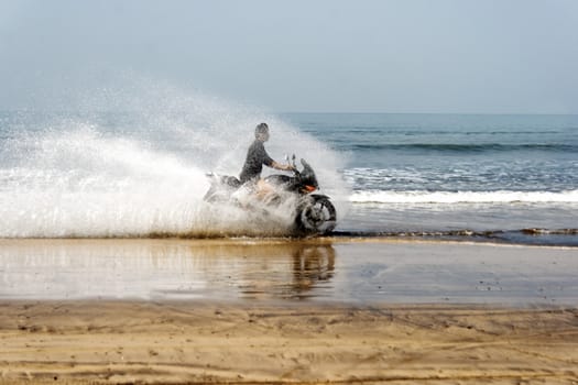 horizontal landscape of lone biker taking pleasure splashing through sea surf on quite beach India with crop margin, copy area and empty spaces