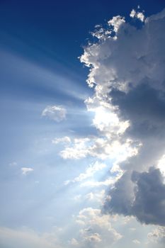 View of white and gray storm clouds in blue sky with rays of light