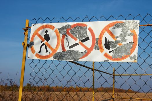 Old table with prohibitive signs and shelled paint hanging on mesh fences in fields