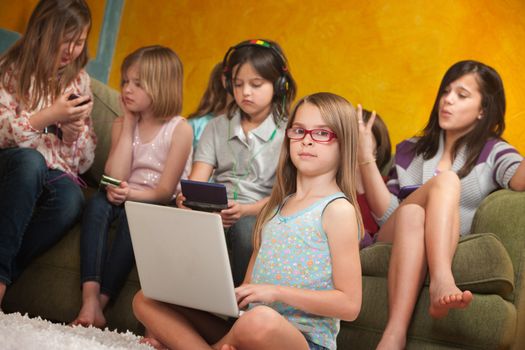 Little girl using laptop while her friends are busy playing on video game consoles