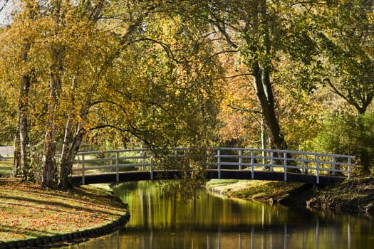 Pond in park in autumn with white bridge and colorful trees