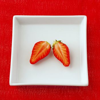Two halves of strawberry, over a white plate, over a red cloth