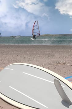 surfboard lying on the beach as surfers windsurf in the maharees in county kerry ireland during a storm