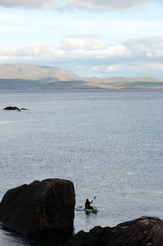 a lone green kayaker on the coast of kerry in ireland