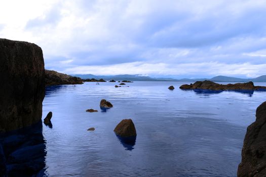 scenic view in kerry ireland of rocks and sea with mountains against a beautiful blue cloudy sky
