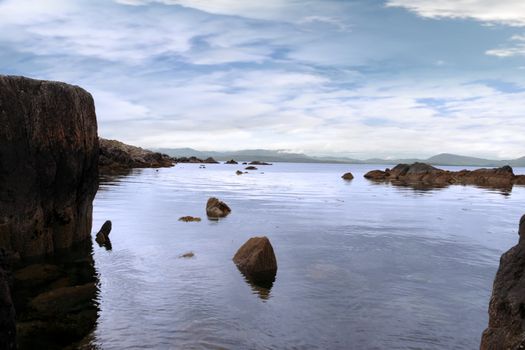 scenic view in kerry ireland of rocks and sea with mountains against a beautiful blue cloudy sky