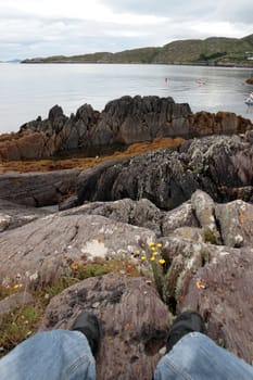a lone hiker on the edge of the coast of kerry in ireland watching kayakers