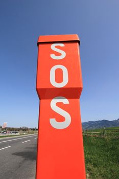 SOS orange sign next to a road by beautiful weather