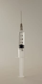 Syringe with little drop on top of needle, over gray background