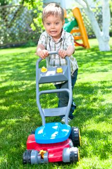 Happy little boy with lawn mower in the garden