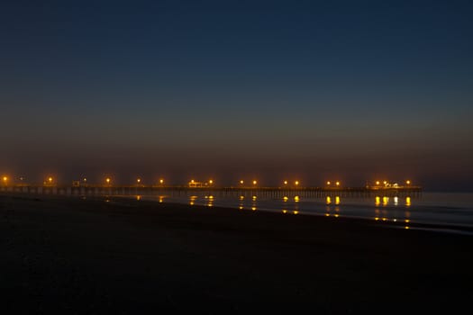 wonderful shot of the sun rising over a pier at an ocean beach