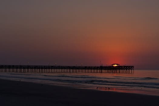 wonderful shot of the sun rising over a pier at an ocean beach