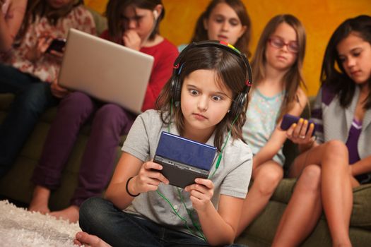Wide-eyed little girl with headphones and game console with friends