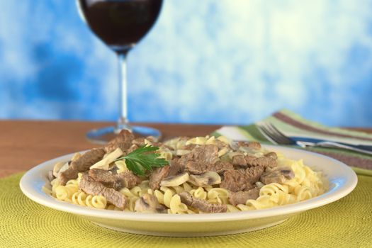 Veal strips with mushrooms and onions in cream sauce served on fusilli pasta and garnished with a parsley leaf (Selective Focus, Focus on the parsley leaf and its surroundings)
