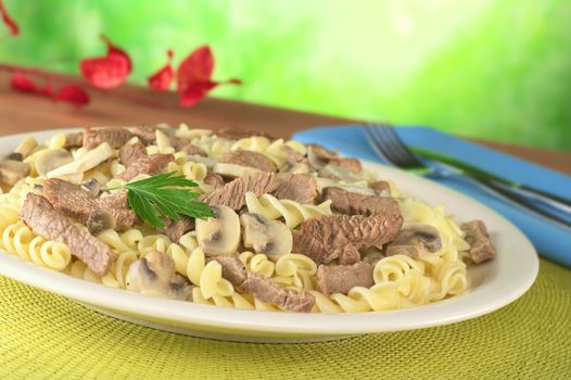 Veal strips with white mushrooms and onion in cream sauce served on fusilli pasta and garnished with a parsley leaf (Selective Focus, Focus on the parsley leaf and its surroundings)