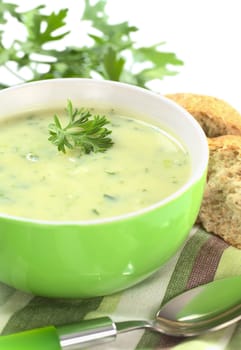 Cream of potato with herbs and green onions garnished with parsley and served in a green bowl with bun and parsley (Selective Focus, Focus on the front of the parsley in the soup)
