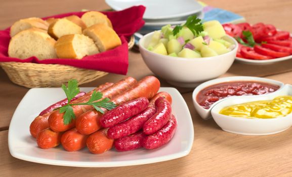 Two types of sausages with ketchup, mustard, potato salad, baguette and tomato slices (Selective Focus, Focus on the front of the sausages)