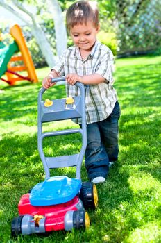 Happy little boy with lawn mower in the garden