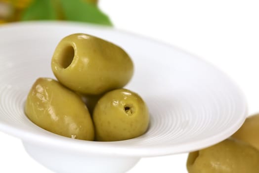 Green olives in a small bowl with olives lying beside (Very Shallow Depth of Field, Focus on the front close to the opening of the top olive)