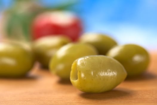 Green olives on wood with blue background (Very Shallow Depth of Field, Focus on the front close to the opening of the front olive)