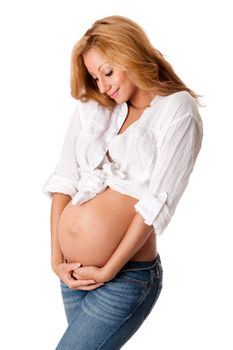 Beautiful new happy mother in late pregnancy wearing fashion jeans and white, looking at tummy holding belly, isolated.