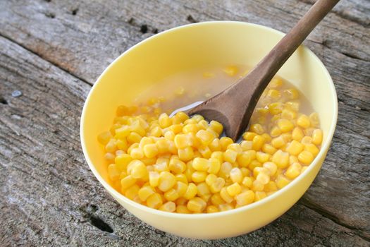 A side dish of corn in a bowl with a wooden spoon and a wooden textured background.