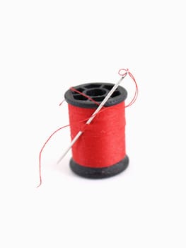 A spool of thread and a needle, isolated on a white background.