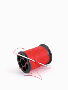 A spool of thread and a needle, isolated on a white background.