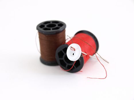 Two spools of thread, a white button and a needle, isolated on a white background.