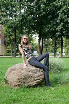 The fashionable girl sits on the big stone