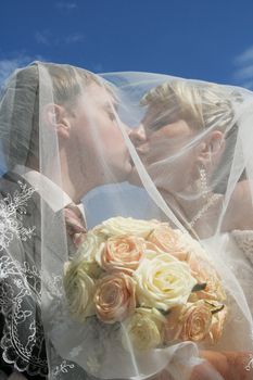 Kiss of a newly-married couple on a background of the blue sky