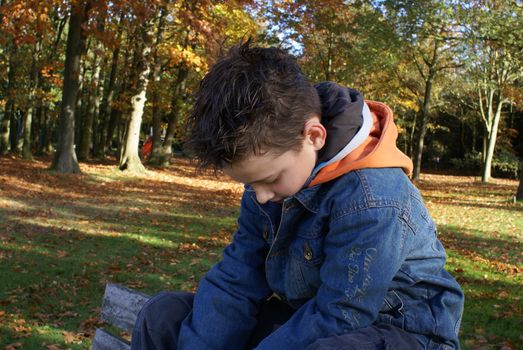 Boy sitting in park staring at the ground.