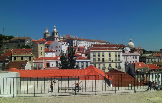 panoramic view of Lisbon´s district Alfama. Abbey Sao Vicente de Fora and the church Santa Engracia ( national pantheon ) in the background, in the foreground some boys skateboarding on the housetops of the tenements