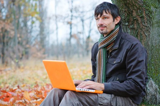 Romantic young man sitting with laptop in the autumn park.