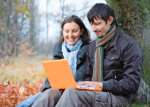Romantic mature couple sitting with laptop in the autumn park.