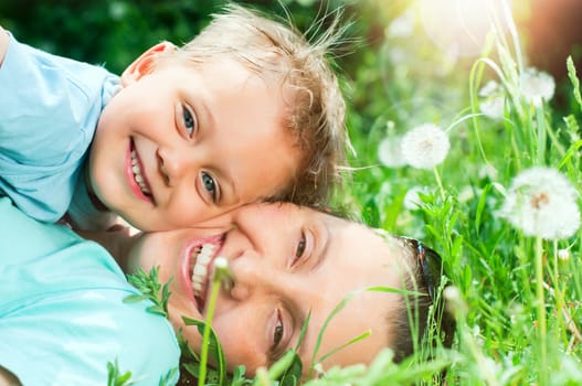 Cute 2 years old boy with mother lying in the grass at sunny summer day