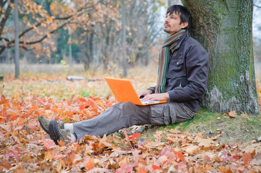 Romantic young man sitting with laptop in the autumn park.