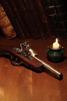 Lighting candle near ancient pistol on wooden surface with old books