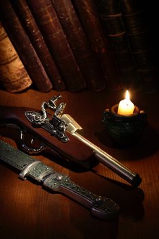 Lighting candle near ancient pistol and dagger on wooden surface with old books