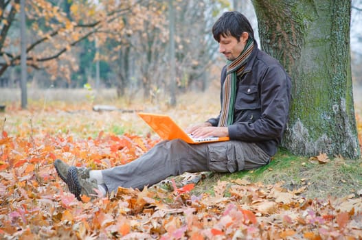 Romantic young man sitting with laptop in the autumn park.